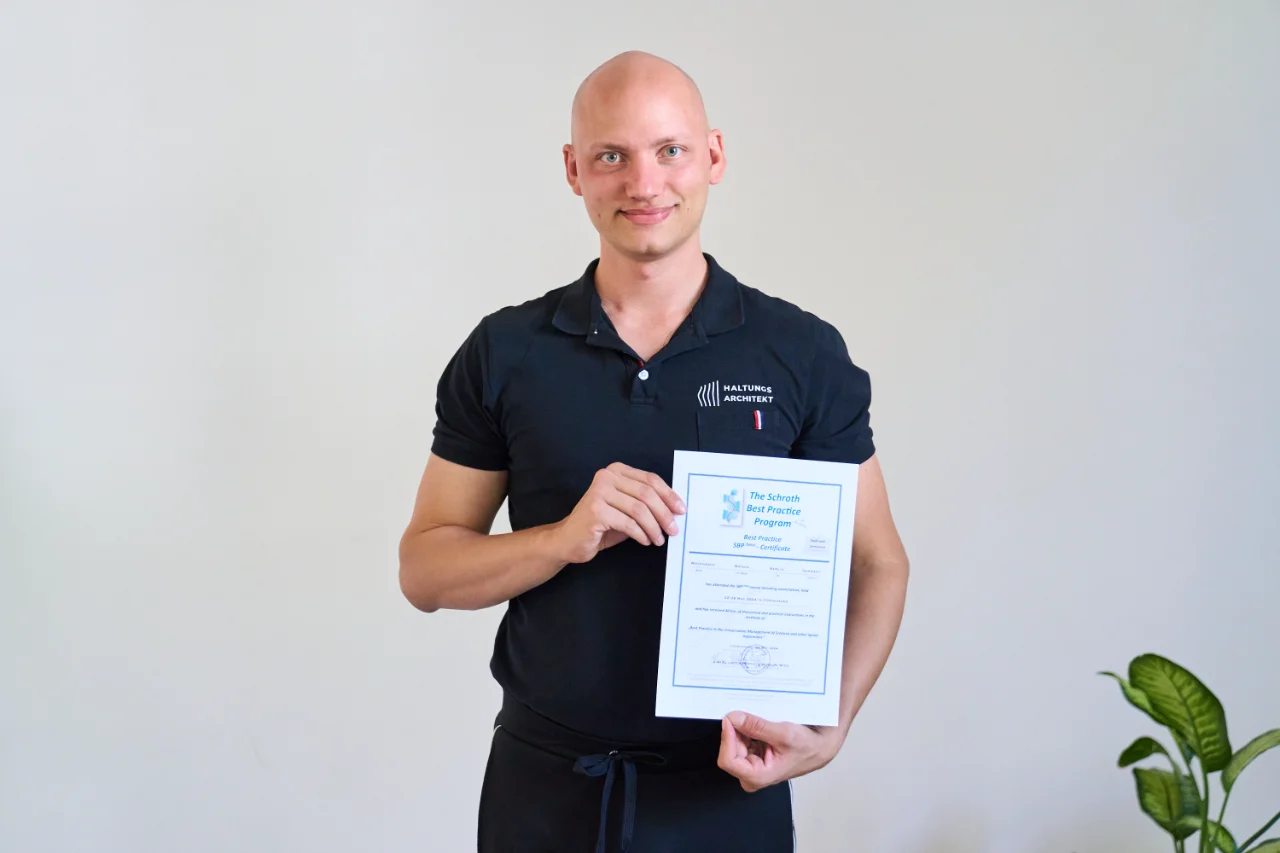 Personal Trainer hält Zertifikat für Skoliose-Spezialisierung in der Hand.